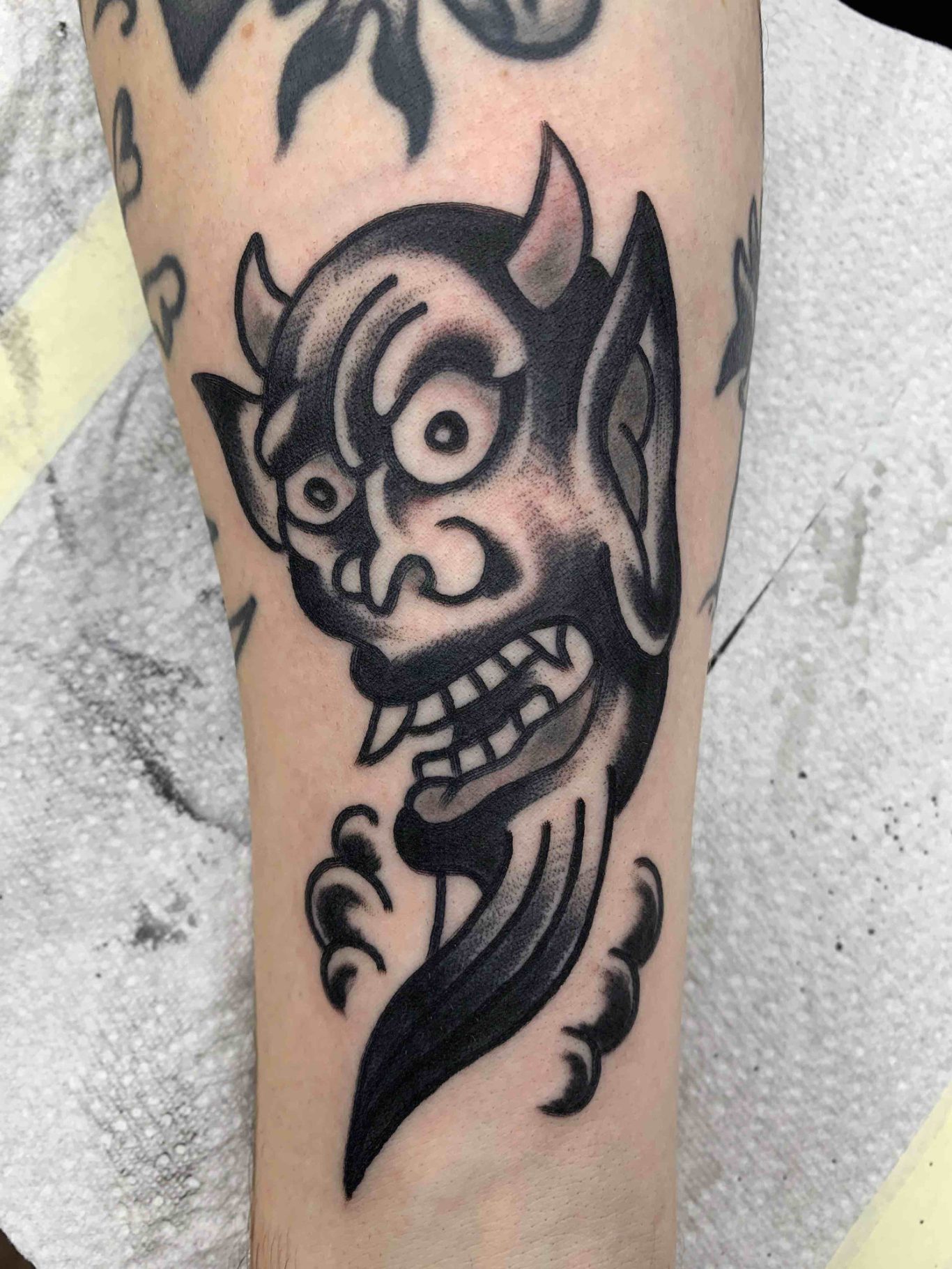 Traditional tattoo Berlin - tattoos by Mariano - Dämonisches Gesicht mit spitzen Ohren und weit geöffnetem Mund auf einem Unterarmtattoo.