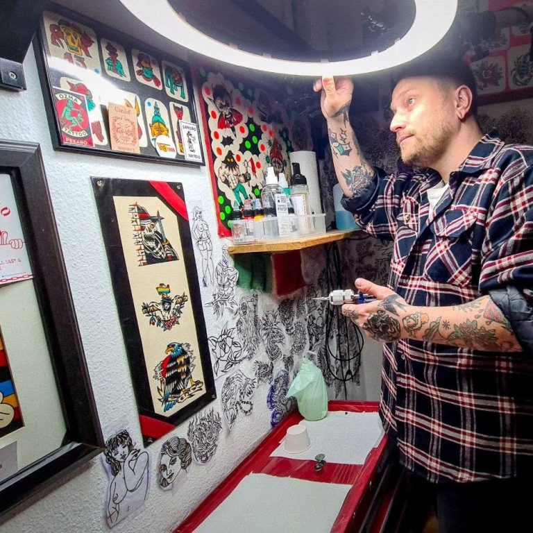 Traditional tattoo Berlin – Tattoos by Mariano – Tattoo artist working at a table surrounded by tattoo designs.