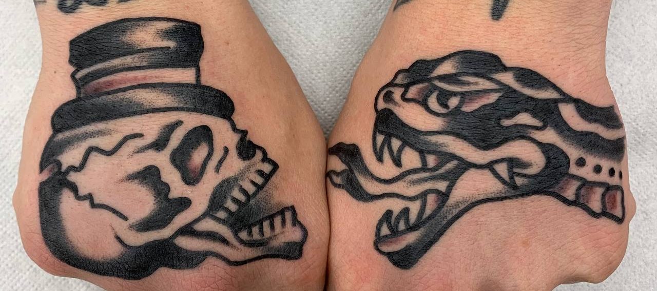 Traditional tattoo Berlin – Tattoos by Mariano – Zwei Hände mit Tattoos: ein Totenschädel mit Zylinder und eine Schnauze eines Raubtiers.