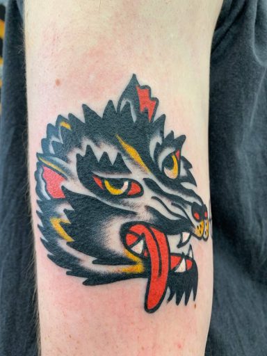 traditional tattoo artists in Berlin - Tattoos by Mariano - Tattoo eines Wolfsgesichts mit roter Zunge und aggressivem Ausdruck.