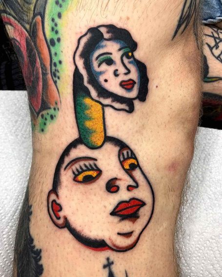 Buntes Tattoo auf einem Bein mit zwei stilisierten Gesichtern und einem grünen Element.