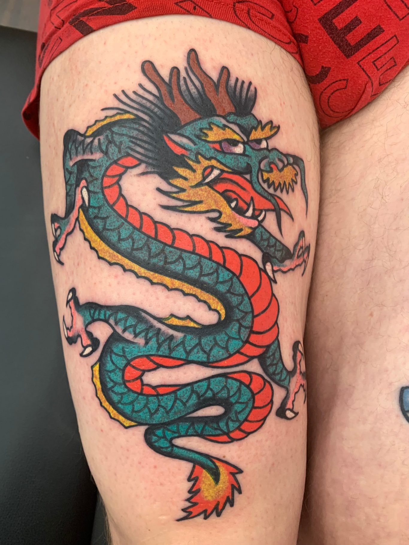 DRAGON Traditional Tattoo Berlin - Tattoos by Mariano - Bunter Tattoo eines Drachen mit detaillierten Schuppen und furchterregendem Gesicht.