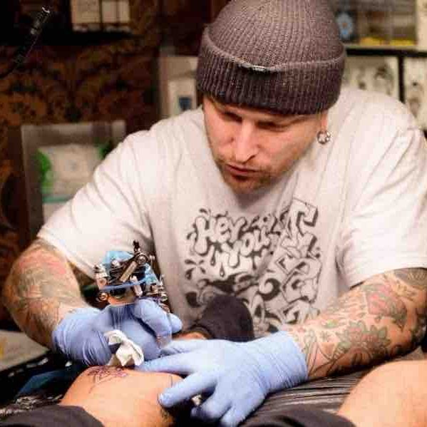 Traditional tattoo Berlin – Tattoos by Mariano – Tattoo artist working at a table surrounded by tattoo designs.