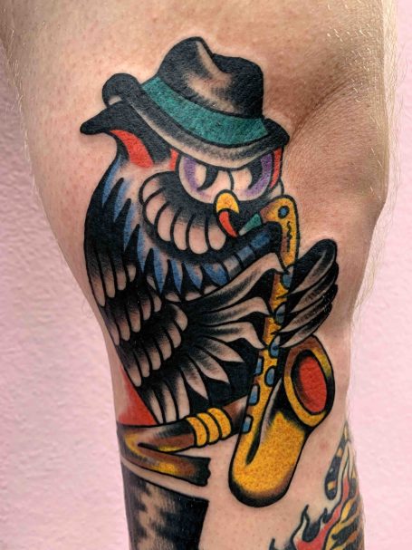 Tattoo eines Eulensaxophonisten mit Hut und Brille auf einem Unterarm.
