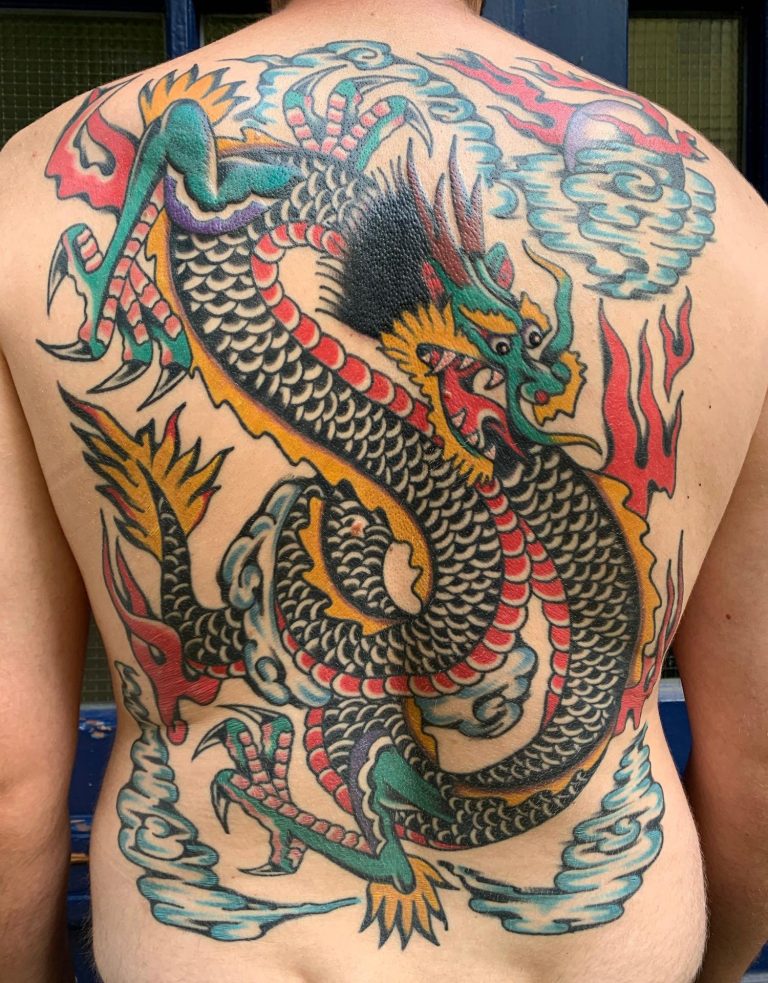 Traditional Tattoo Berlin - Tattoos by Mariano - Bunt tätowierter Drache auf dem Rücken, umgeben von Wolken und Flammen.