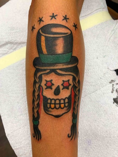 Traditional tattoo Berlin - Tattoos by Mariano - Bunt gestaltetes Tattoo eines Schädels mit Zylinder und geflochtenen Zöpfen.