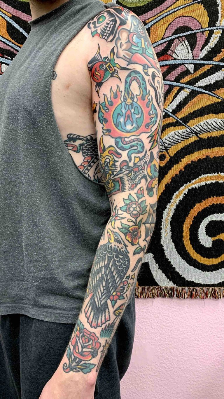 Traditional Tattoo Berlin - Tattoos by Mariano - Colorful traditional tattoo arm sleeve with various motifs, next to a patterned background.