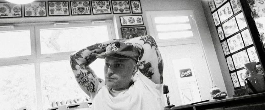 Ein Tätowierer arbeitet an einem tätowierten Mann auf einem Tisch in einem Tattoo-Studio.