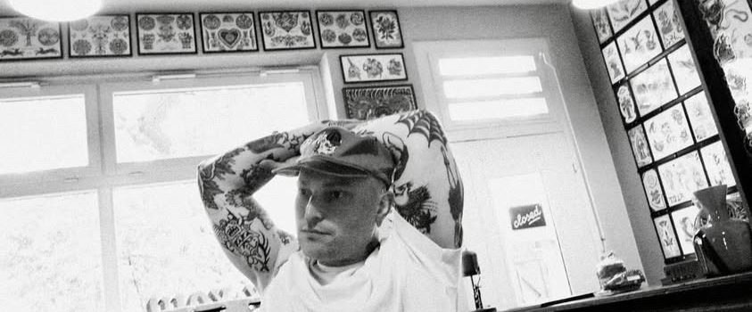 Traditional tattoo Berlin – Tattoos by Mariano – A tattoo artist works on a tattooed man lying on a couch in a studio.